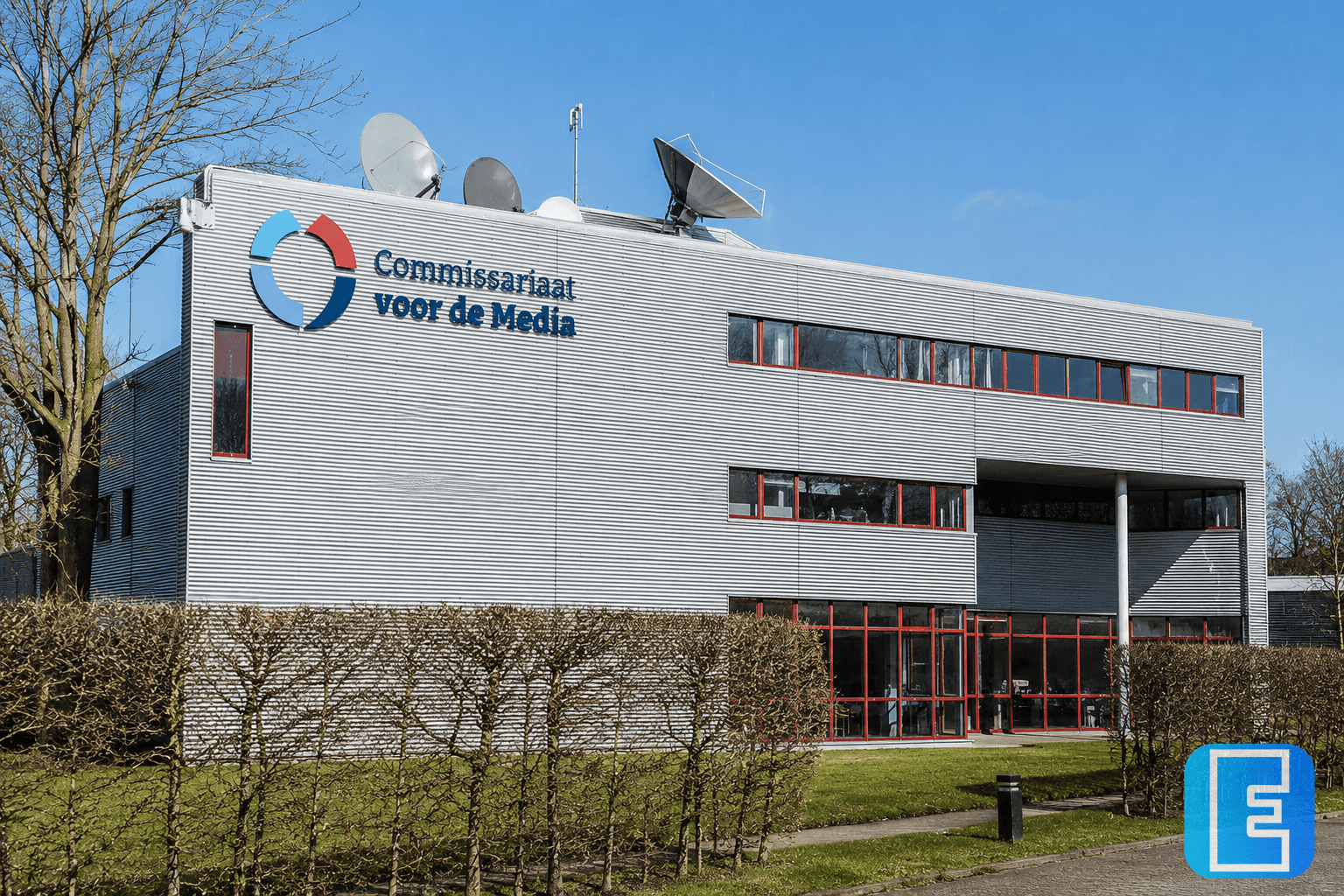 Een modern kantoorgebouw met gevelbelettering van het Commissariaat voor de Media. Voor het gebouw staan gesnoeide hagen en bomen; op het dak zijn meerdere schotelantennes zichtbaar.