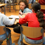 Drie studenten overleggen aan een tafel in een klaslokaal